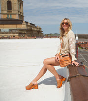 Woman sitting on a Bed Stu Vanquish platform with a cityscape background on a sunny day.