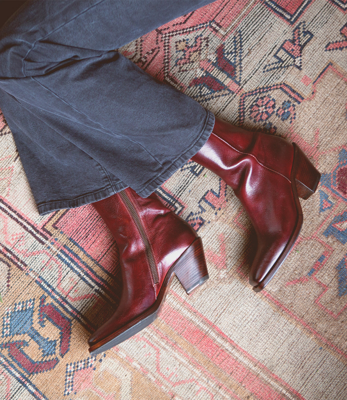 A woman donning a pair of Bed Stu Vendue high-quality leather red boots with a sleek silhouette on a cozy rug.