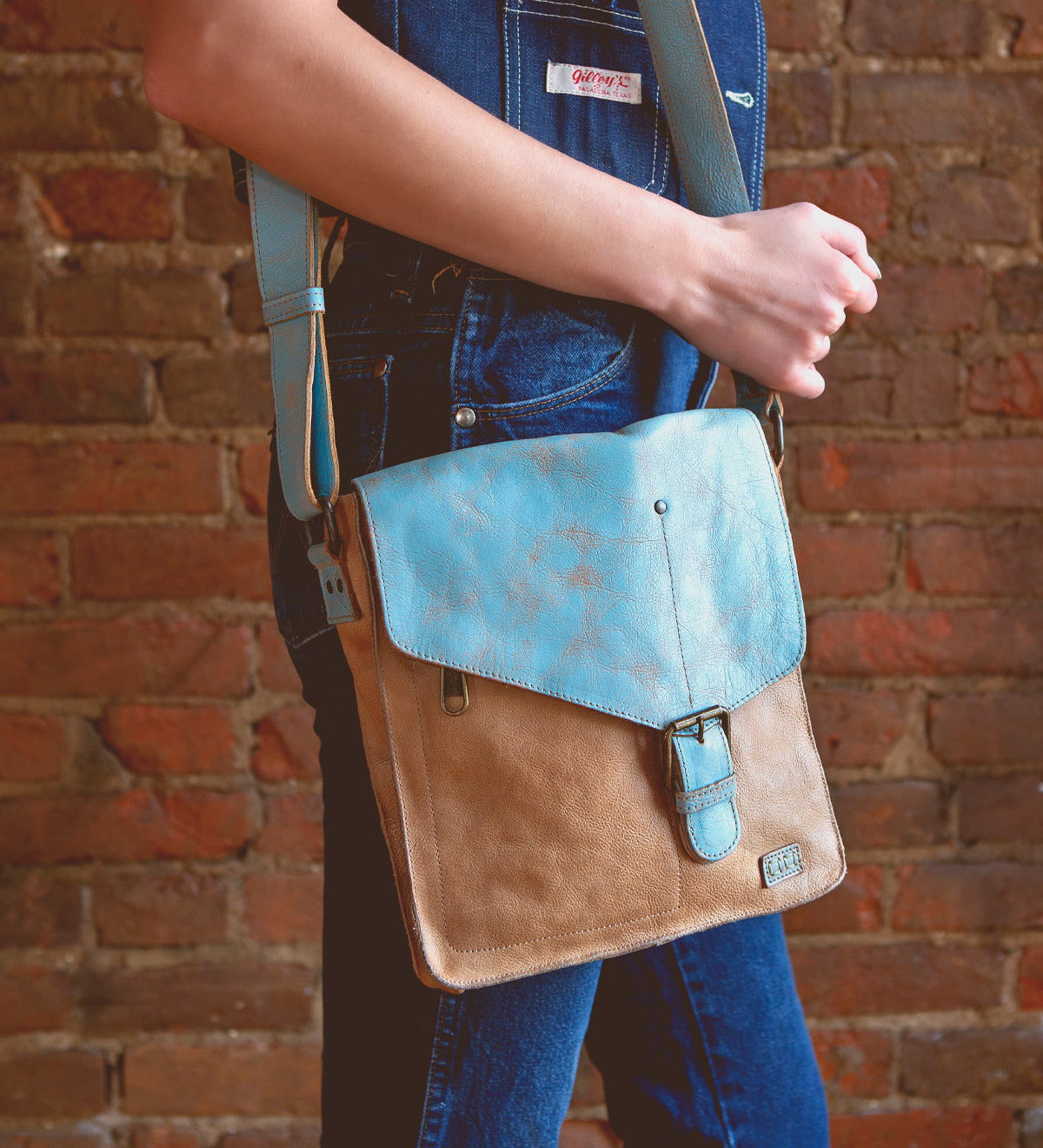 A woman is holding a Bed Stu Venice Beach, a vintage-inspired leather crossbody bag.