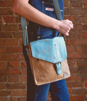A woman is holding a Bed Stu Venice Beach, a vintage-inspired leather crossbody bag.