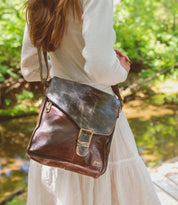 A person stands by a stream, carrying the Venice Beach crossbody bag by Bed Stu, showcasing quality craftsmanship.