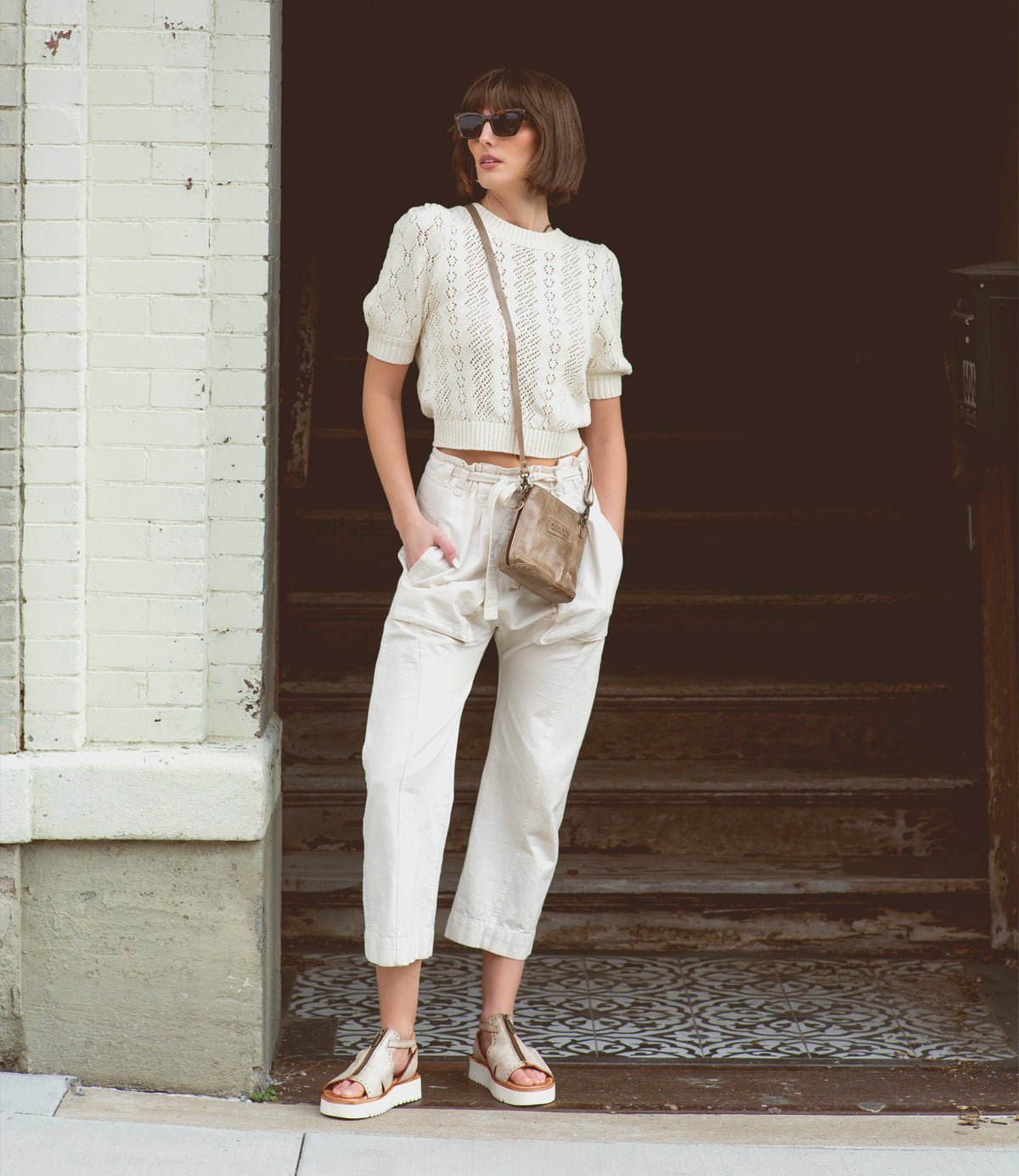 A woman wearing a white sweater and white pants accessorized with a Bed Stu Ventura leather cross body bag.