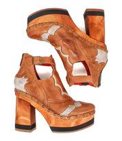 The Bed Stu Viretta is a stylish pair of brown leather platform heels, featuring chunky handcrafted wooden soles, decorative stitching, and metal studs for a fashionable vintage look.