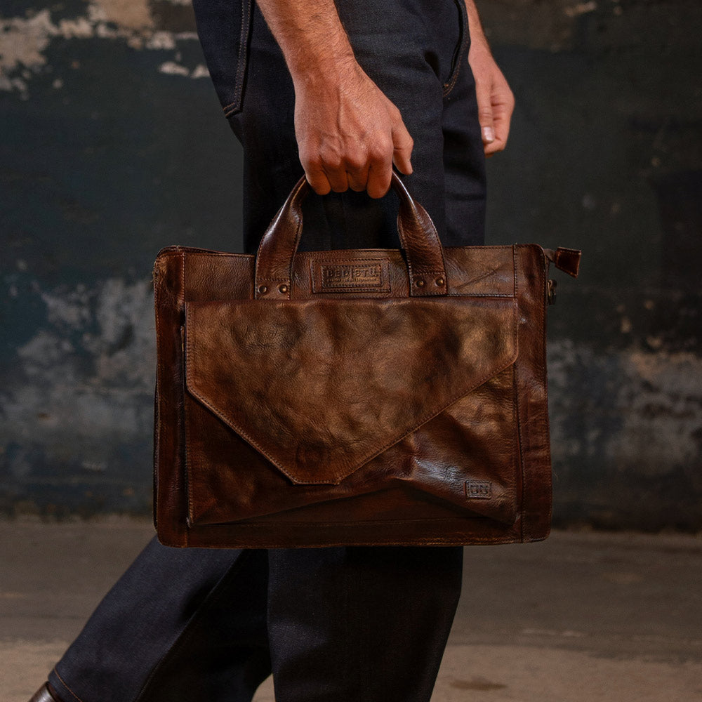 Person carrying a brown leather briefcase-style bag with top handles and a front envelope pocket.