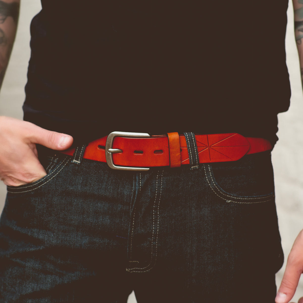 A person wearing a black shirt, dark jeans, and a brown leather Bed Stu Westham belt with a removable silver buckle featuring a stamped star design, shown from the waist down.
