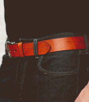 Close-up of a person wearing dark jeans with a plain black shirt, featuring a Bed Stu Westham brown leather belt with a stamped star design and a silver removable buckle.