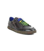 The Bed Stu Wizard is a dark brown, low-profile leather sneaker with crossover stitching, blue inner lining, and multi-colored laces in blue, purple, green, and yellow, shown at an angle on a white background.