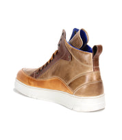 The Bed Stu Workbench is a men’s brown leather sneaker with a white cushioned rubber sole and blue interior lining, featuring a versatile design, shown from the back-left angle.
