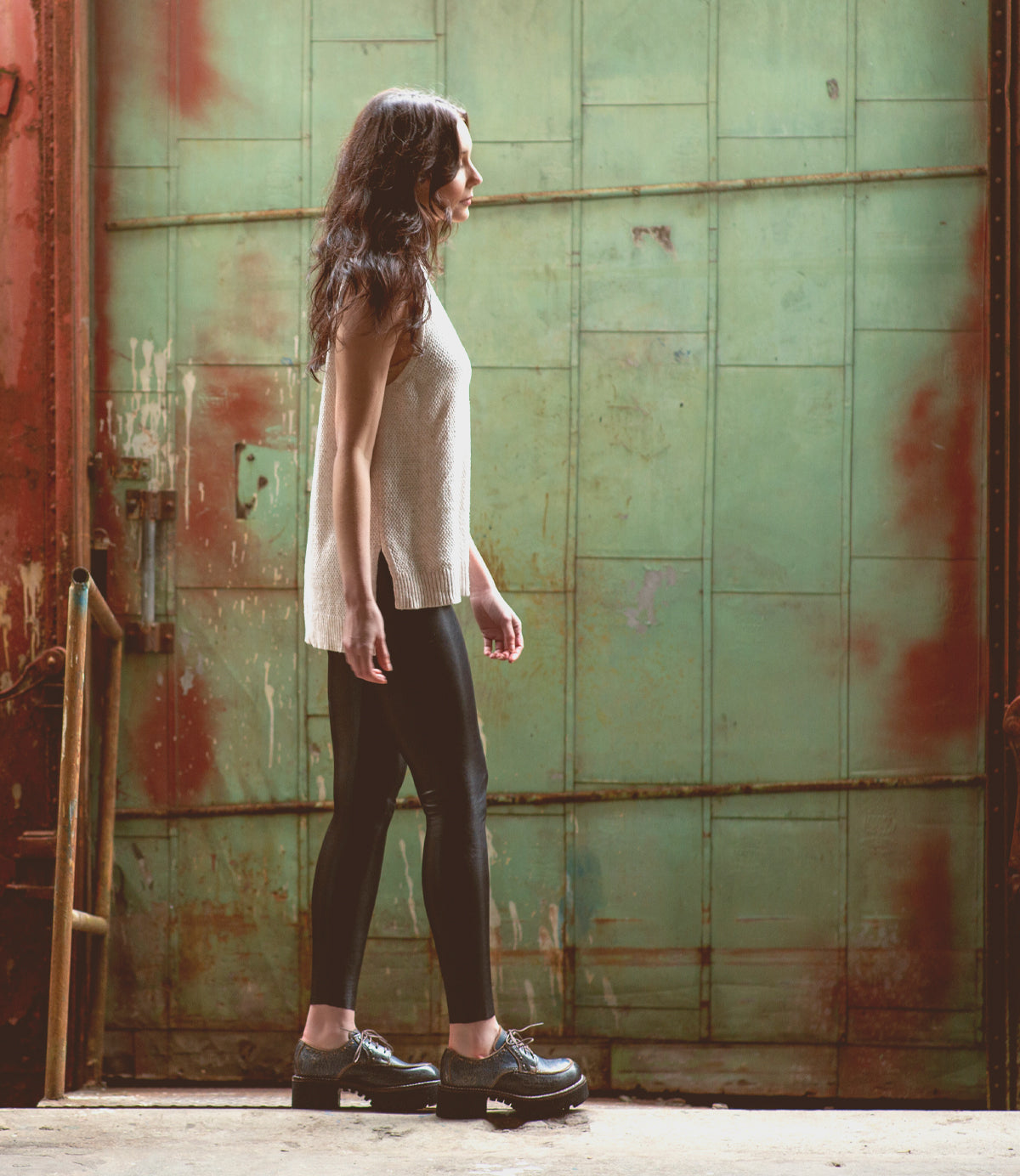 A woman wearing Bed Stu Yazar platform lace-up leather shoes standing in front of a green building.