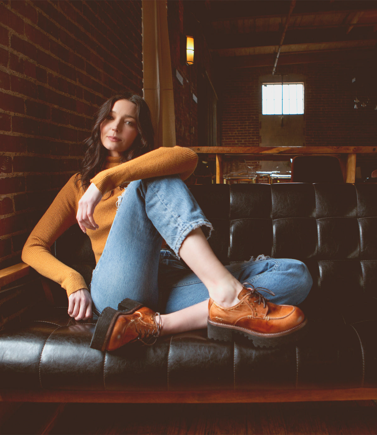 A woman sitting on a black leather couch wearing Bed Stu Yazar platform lace-up shoes.