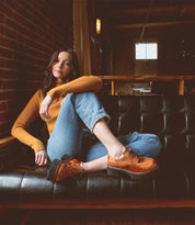 A woman sitting on a black leather couch wearing Bed Stu Yazar platform lace-up shoes.