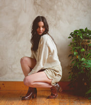 A woman in Bed Stu high-heeled boots crouching down in front of a plant.