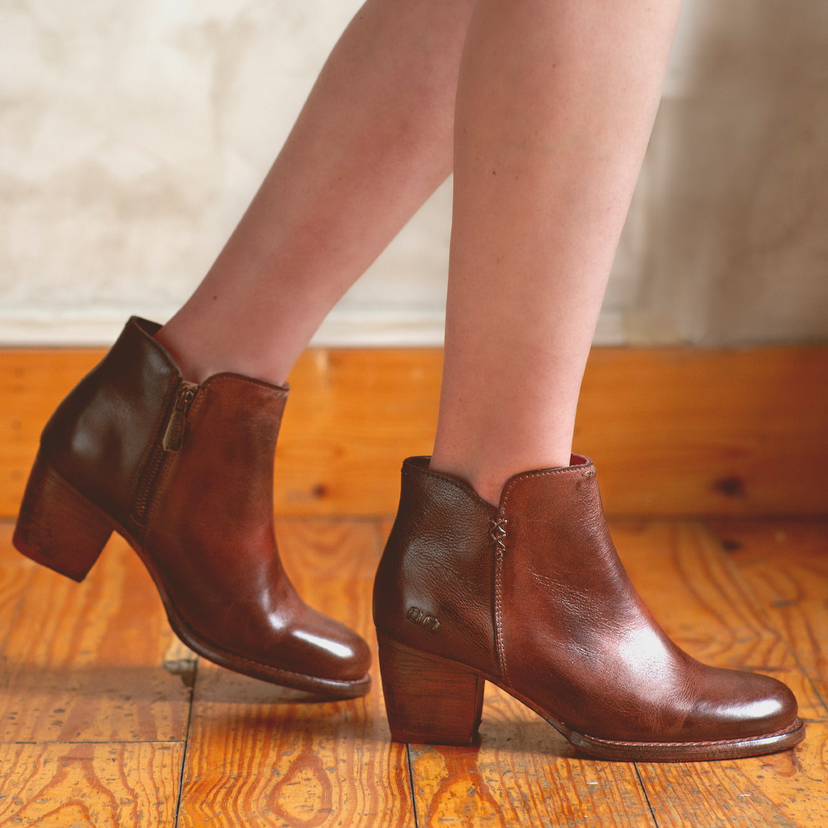 A woman's legs standing on a wooden floor in high-heeled Bed Stu Yell boots.