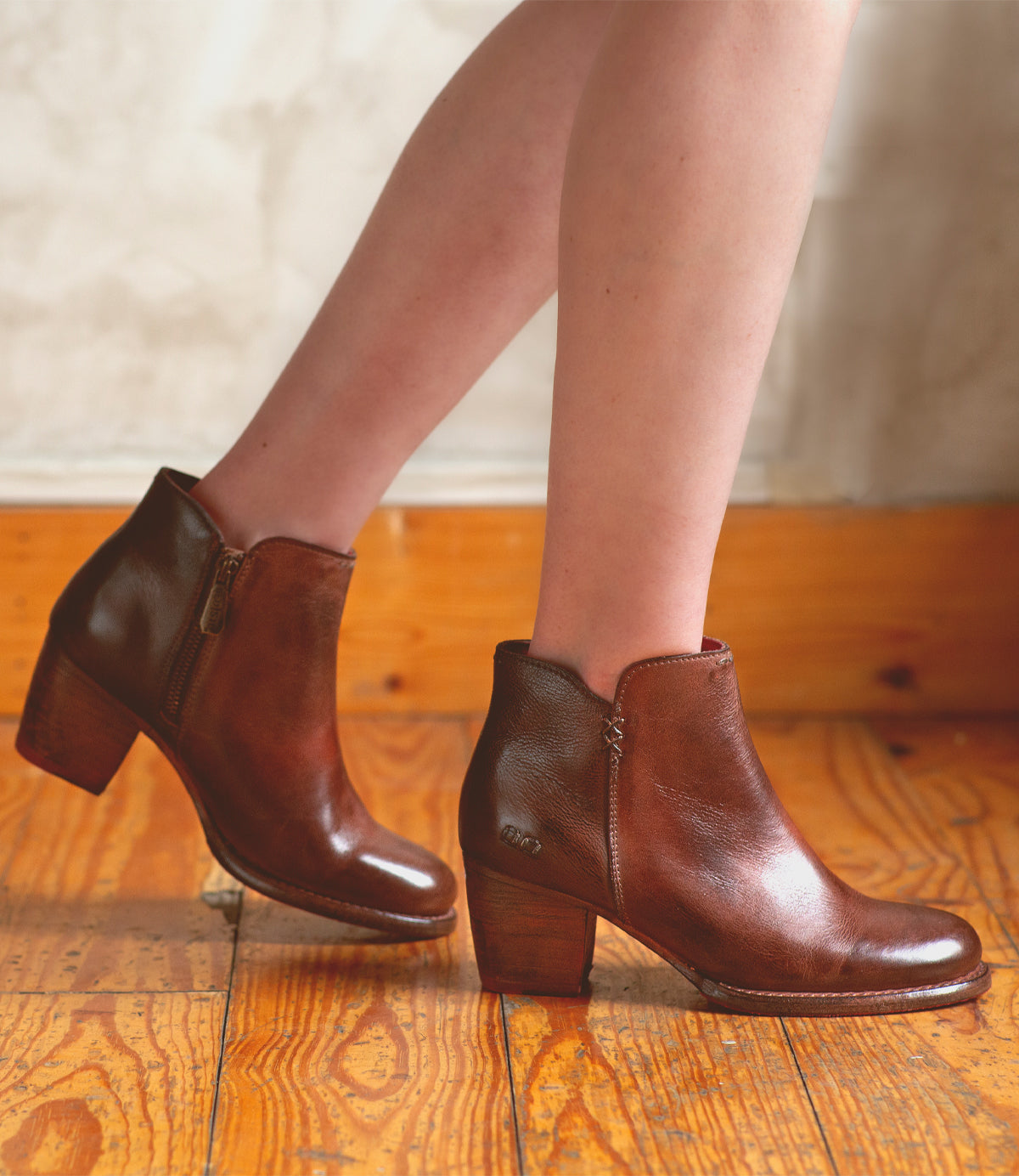 A woman's legs standing on a wooden floor in high-heeled Bed Stu Yell boots.