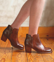 A woman's legs standing on a wooden floor in high-heeled Bed Stu Yell boots.