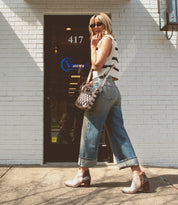 Woman in casual attire standing in front of a building entrance with sunglasses, Bed Stu handmade leather boots, and a shoulder bag.