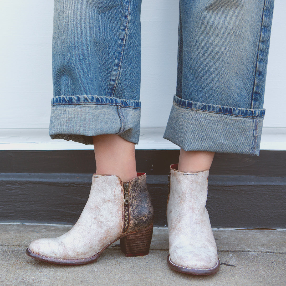 A pair of white, handmade leather boots with distressed ankle design paired with rolled-up denim jeans from Bed Stu's Yell collection.