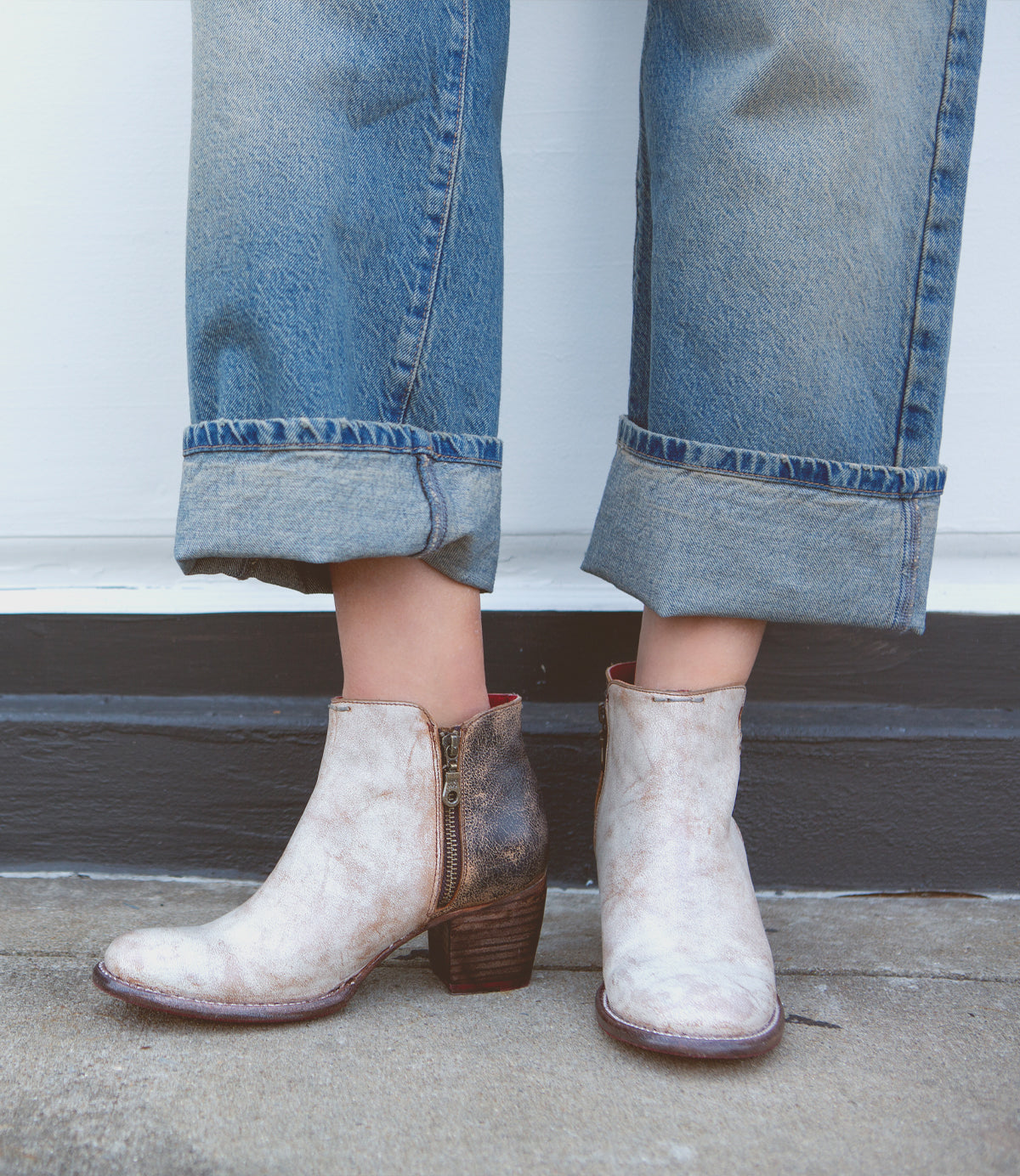 A pair of white, handmade leather boots with distressed ankle design paired with rolled-up denim jeans from Bed Stu's Yell collection.