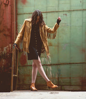 A woman wearing a tan jacket and black dress paired with high-heeled leather Yell boots from Bed Stu.