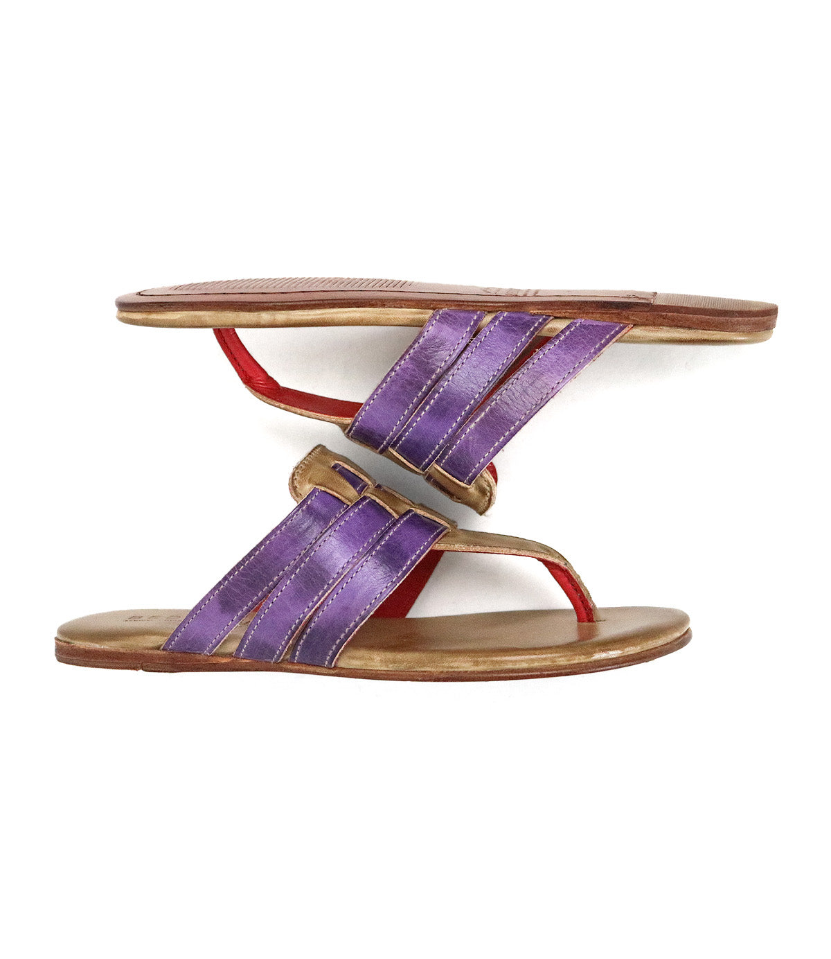 Two Bed Stu Yoli sandals with woven leather uppers in purple and gold are placed sole to sole, with one sandal balanced upside down on top of the other.
