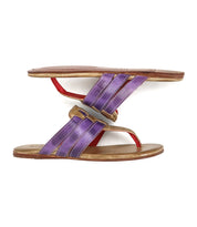 Two Bed Stu Yoli sandals with woven leather uppers in purple and gold are placed sole to sole, with one sandal balanced upside down on top of the other.