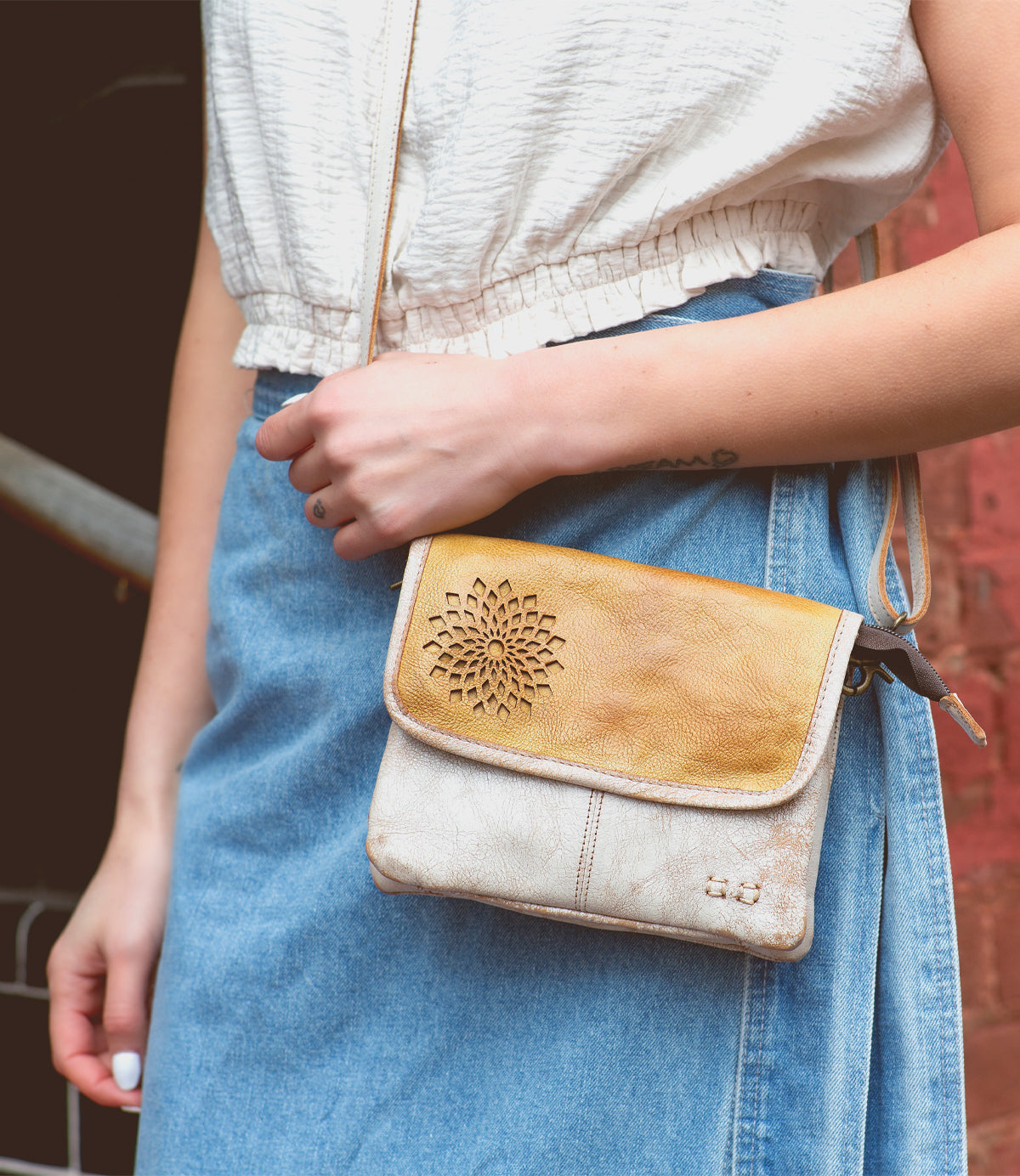 A woman wearing a denim skirt and carrying a stylish Bed Stu Ziggy II crossbody bag with compartments.