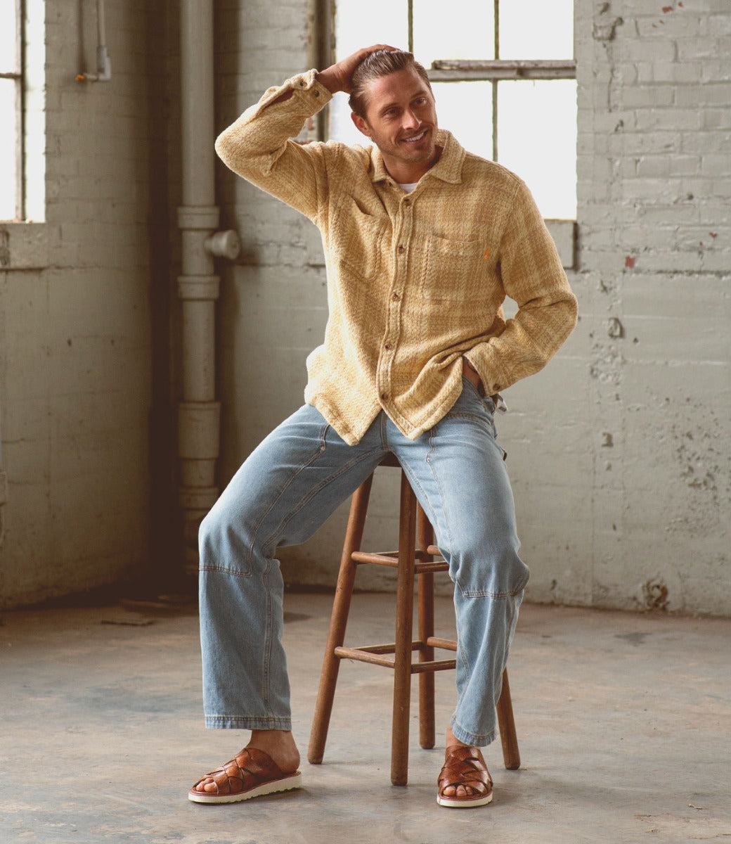 A man sitting on a stool wearing a Bed Stu Abraham Light shirt and jeans.