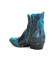 The Ace boot by Bed Stu, a blue and black distressed leather cowboy design with a side zipper and curved low heel, showcases modern western style against a white background. Crafted from durable stacked leather, this boot effortlessly blends rugged durability with contemporary fashion.