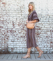 A stylish blonde woman wearing a striped midi dress and carrying a Bed Stu wicker bag.