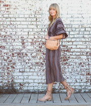 A stylish blonde woman wearing a striped midi dress and carrying a Bed Stu wicker bag.