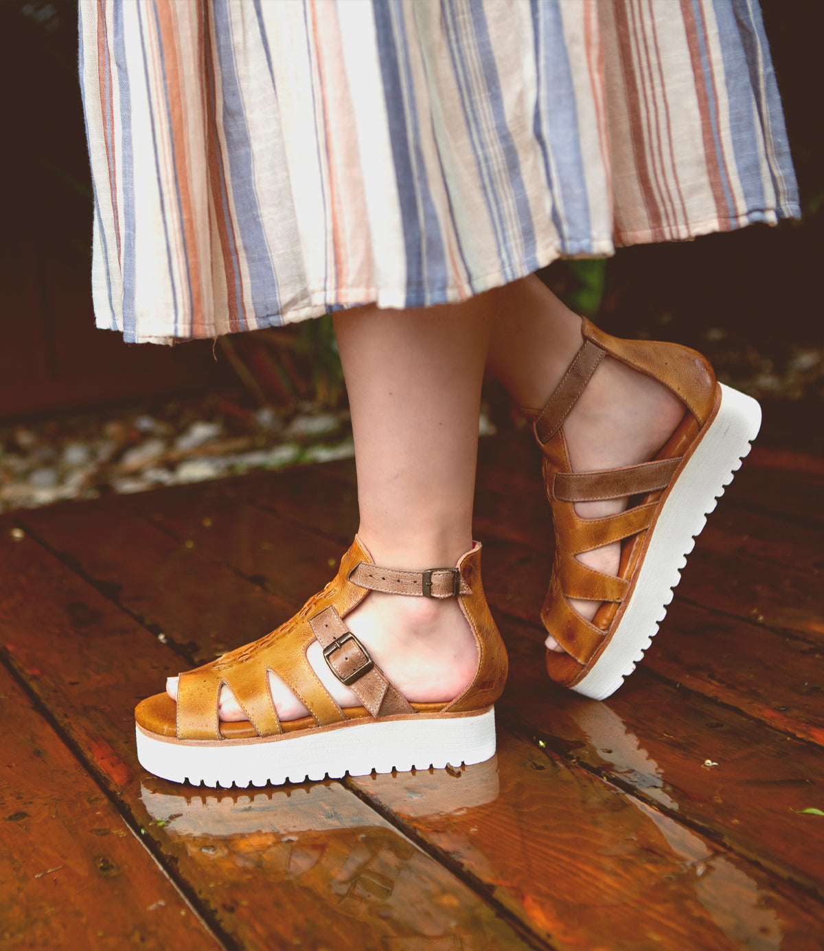 A woman wearing Bed Stu Ada sandals on a wooden deck.