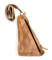 A brown vegetable tanned leather sling bag with a single zippered pocket and an adjustable strap, featuring a small label with the brand name "Bed Stu." This versatile Adept crossbody bag is the perfect travel companion.