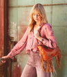 A blonde woman wearing jeans and a fringed Bed Stu purse with vintage-inspired details.