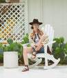 A woman in a cowboy hat sitting on an Afrodita rocking chair by Bed Stu.