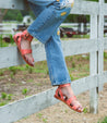 A woman wearing Afrodita jeans and Bed Stu sandals leaning against a fence.