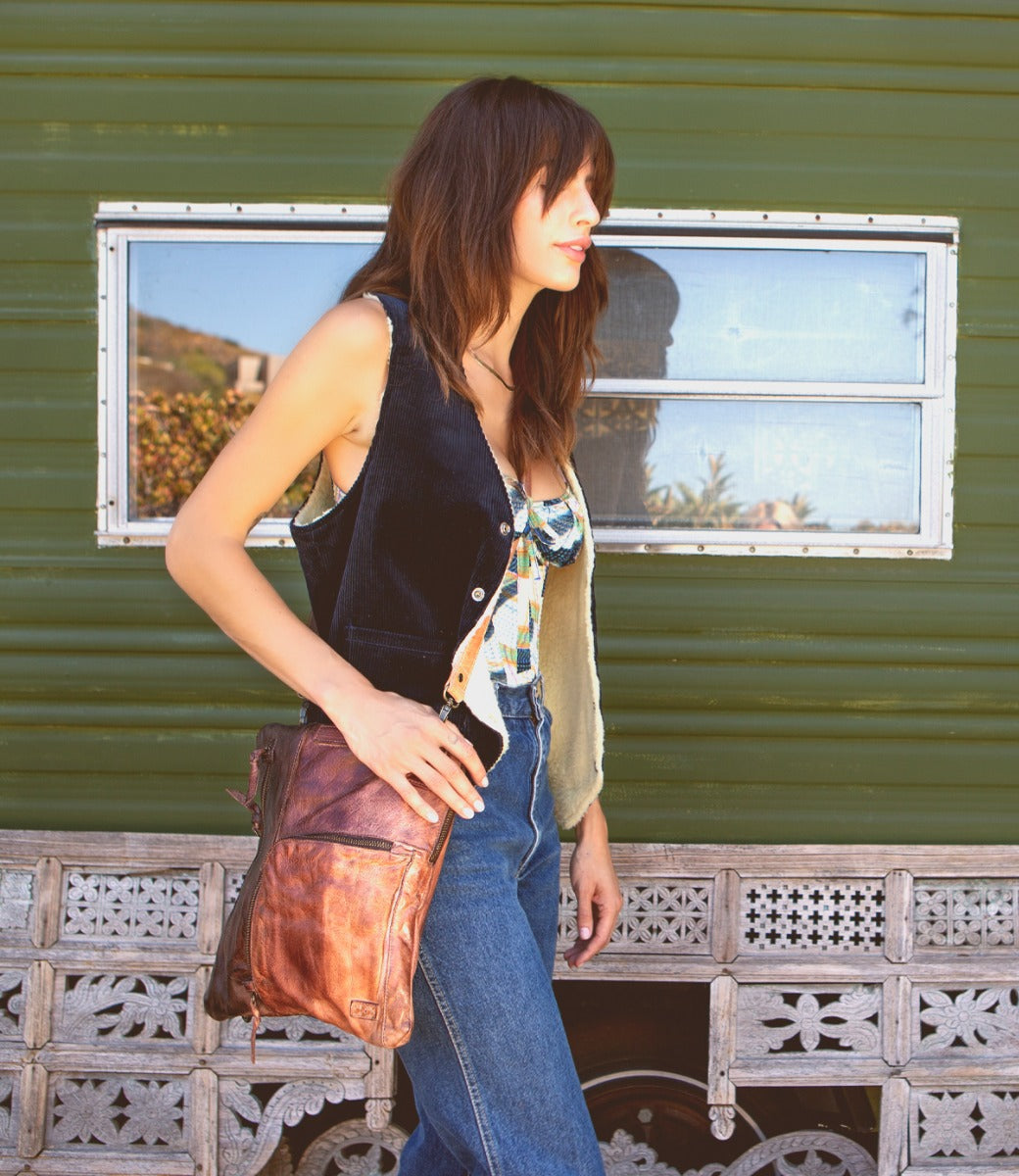 A woman in Aiken jeans and a Bed Stu vest is standing in front of a trailer.