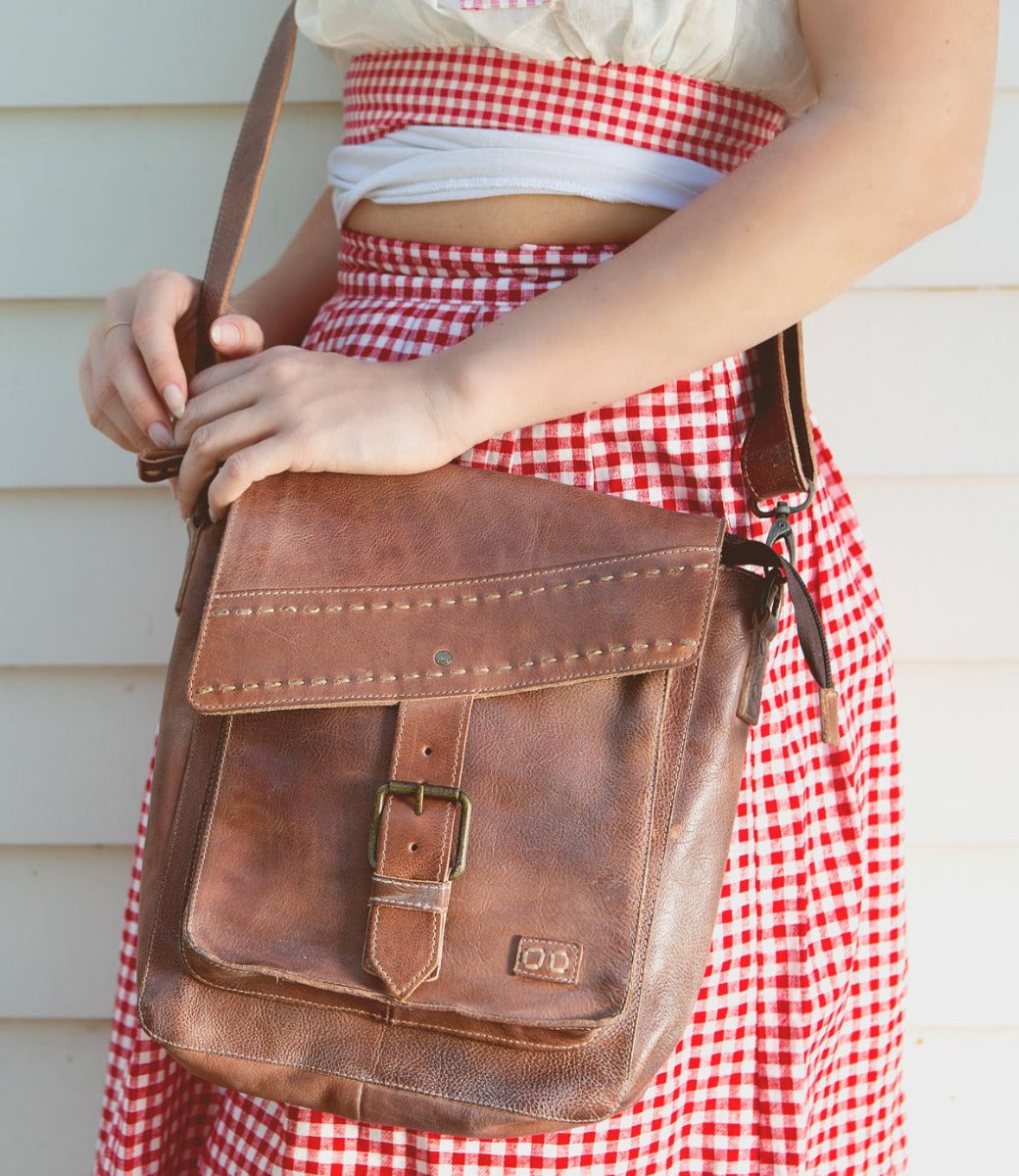 A woman in a red and white skirt holding a Bed Stu Ainhoa brown leather crossbody handbag.