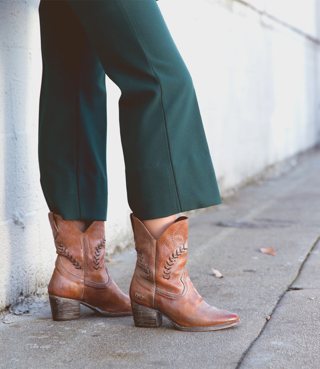 A woman wearing green pants and brown Bed Stu cowboy boots.
