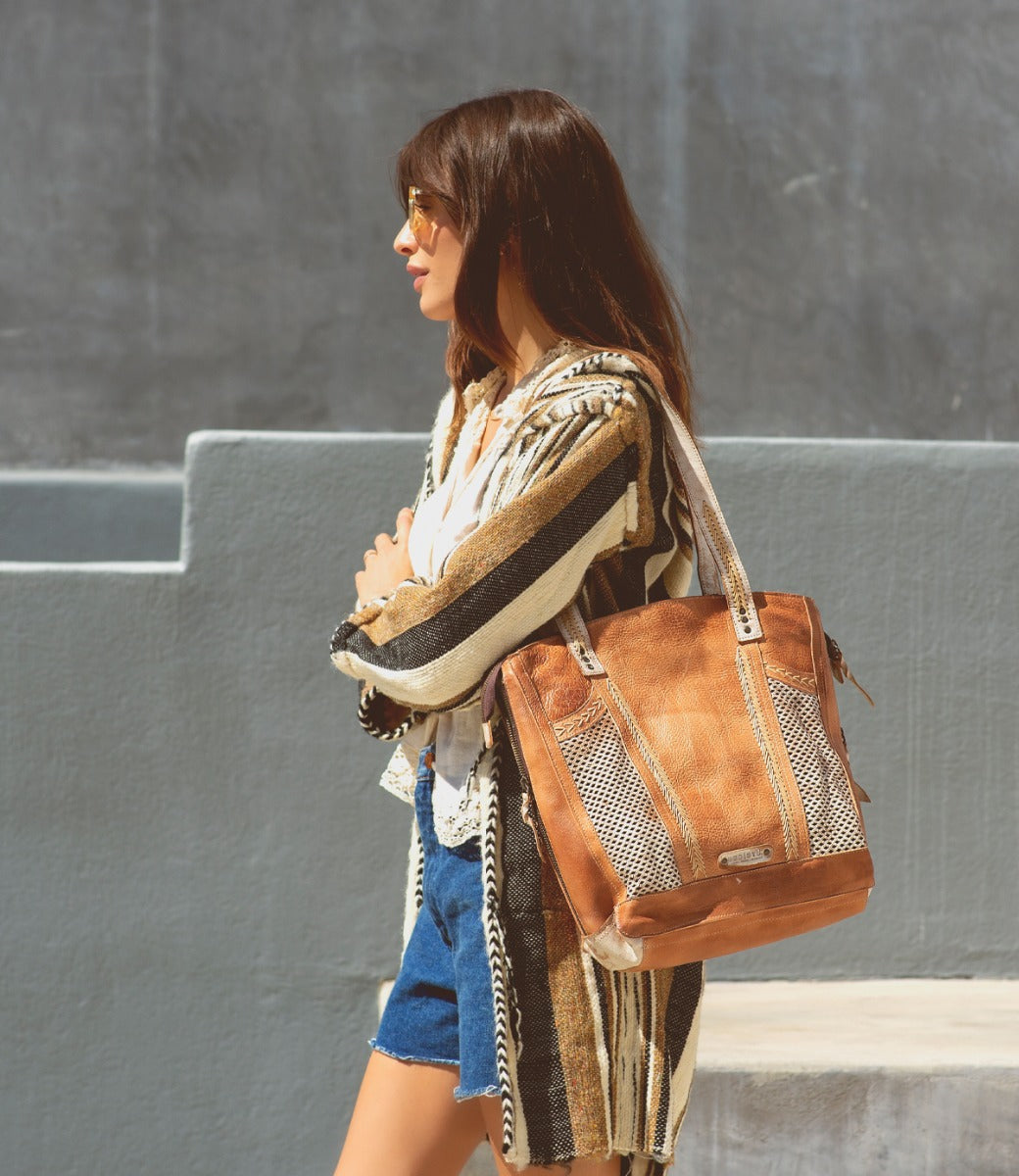 A woman wearing shorts and a striped blazer carrying a Bed Stu Amelie tote bag.