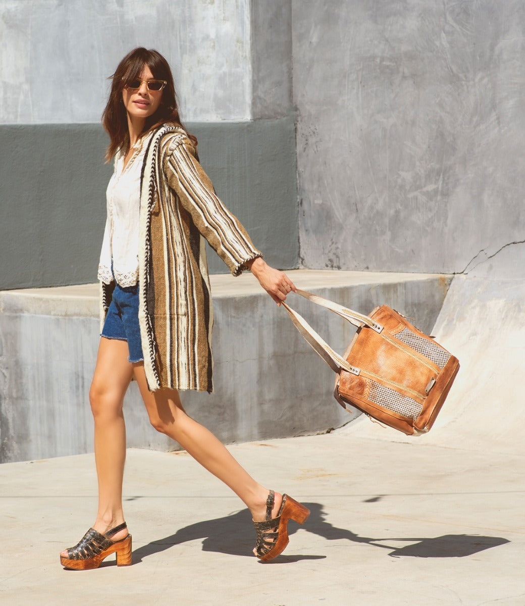 A woman in shorts and a striped jacket walking with an Amelie bag by Bed Stu.