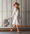 A woman in a white dress and hat walking with an Amelie bag from Bed Stu.