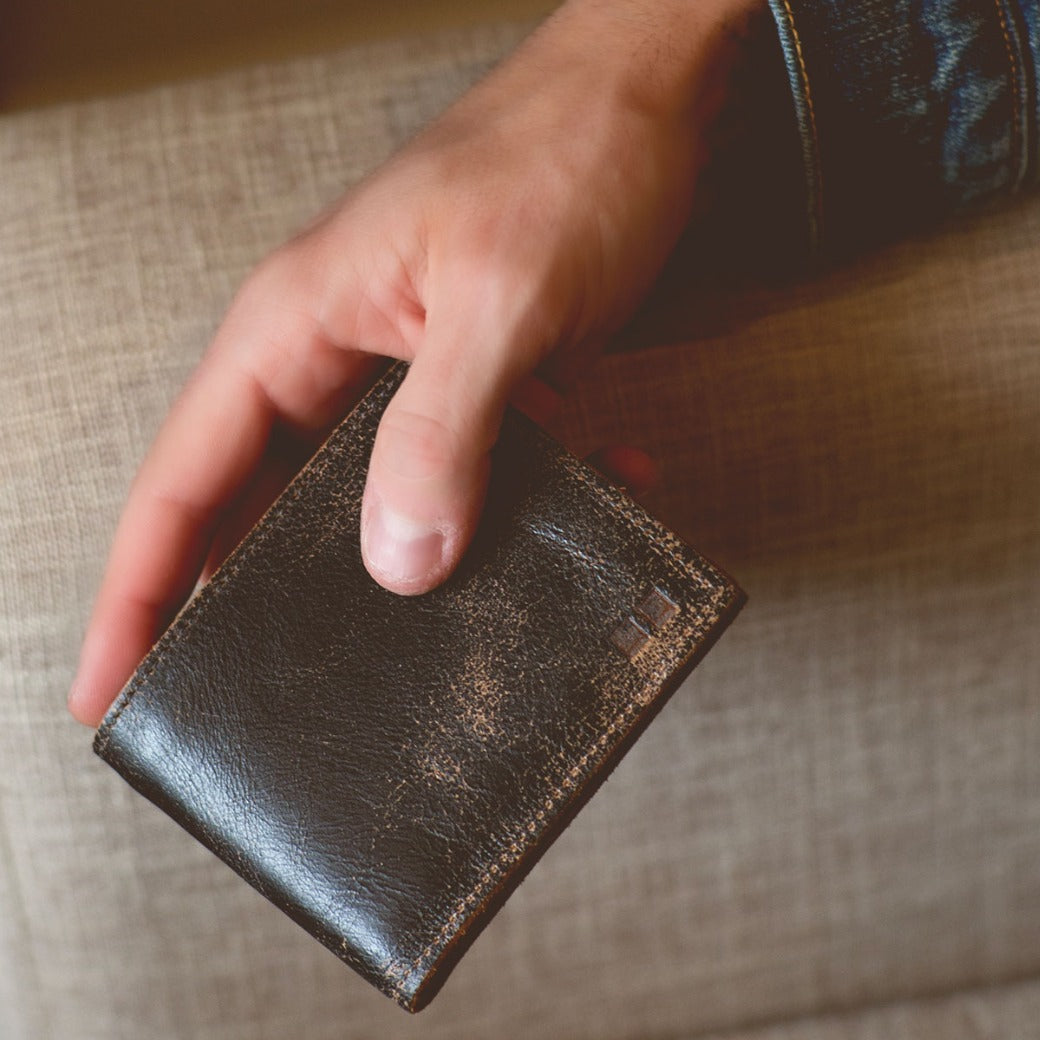 A person holding a black leather Amidala wallet on a couch. (Brand: Bed Stu)