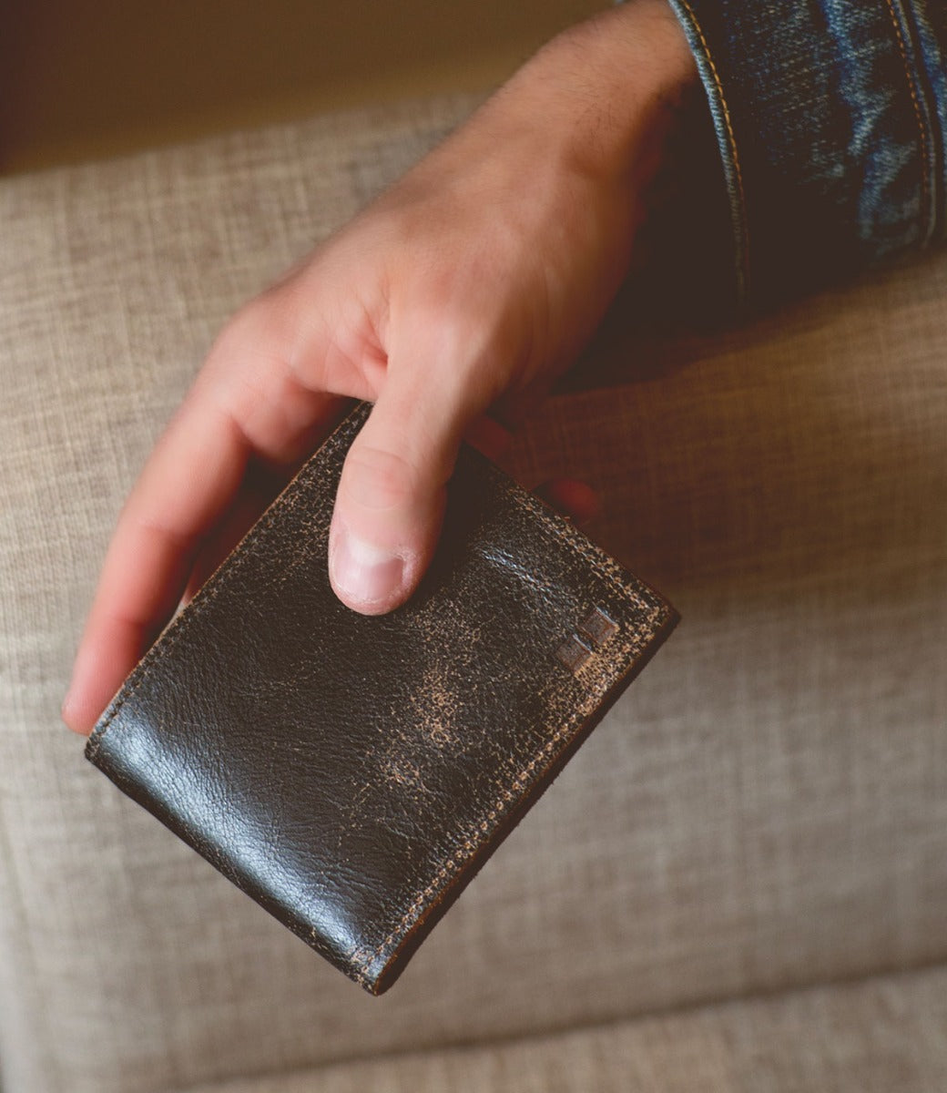 A person holding a black leather Amidala wallet on a couch. (Brand: Bed Stu)