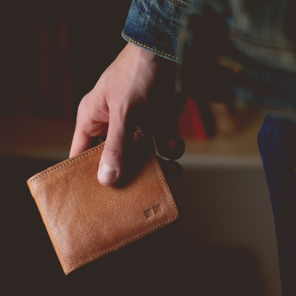 A man holding a Bed Stu Amidala tan leather wallet.