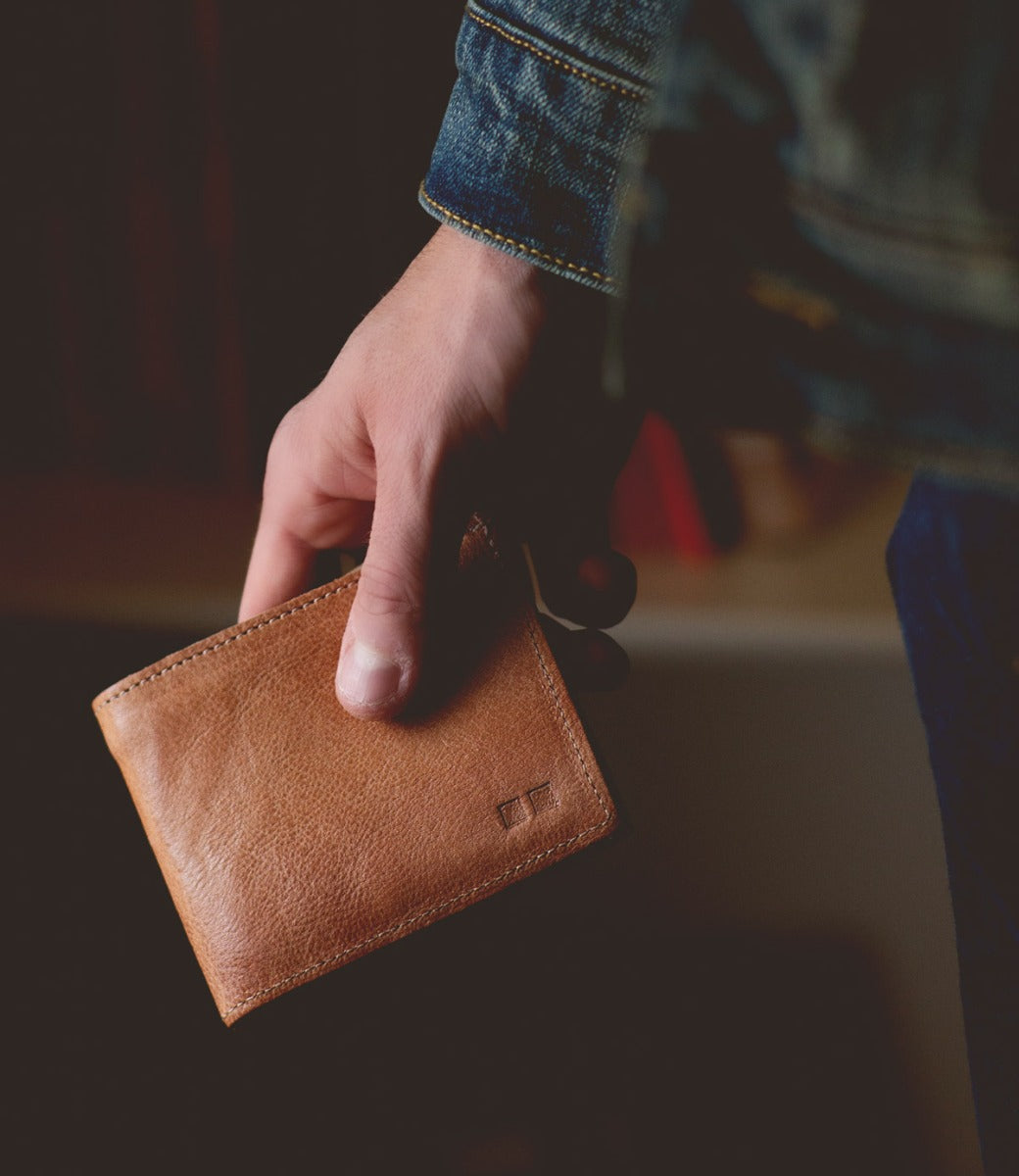 A man holding a Bed Stu Amidala tan leather wallet.