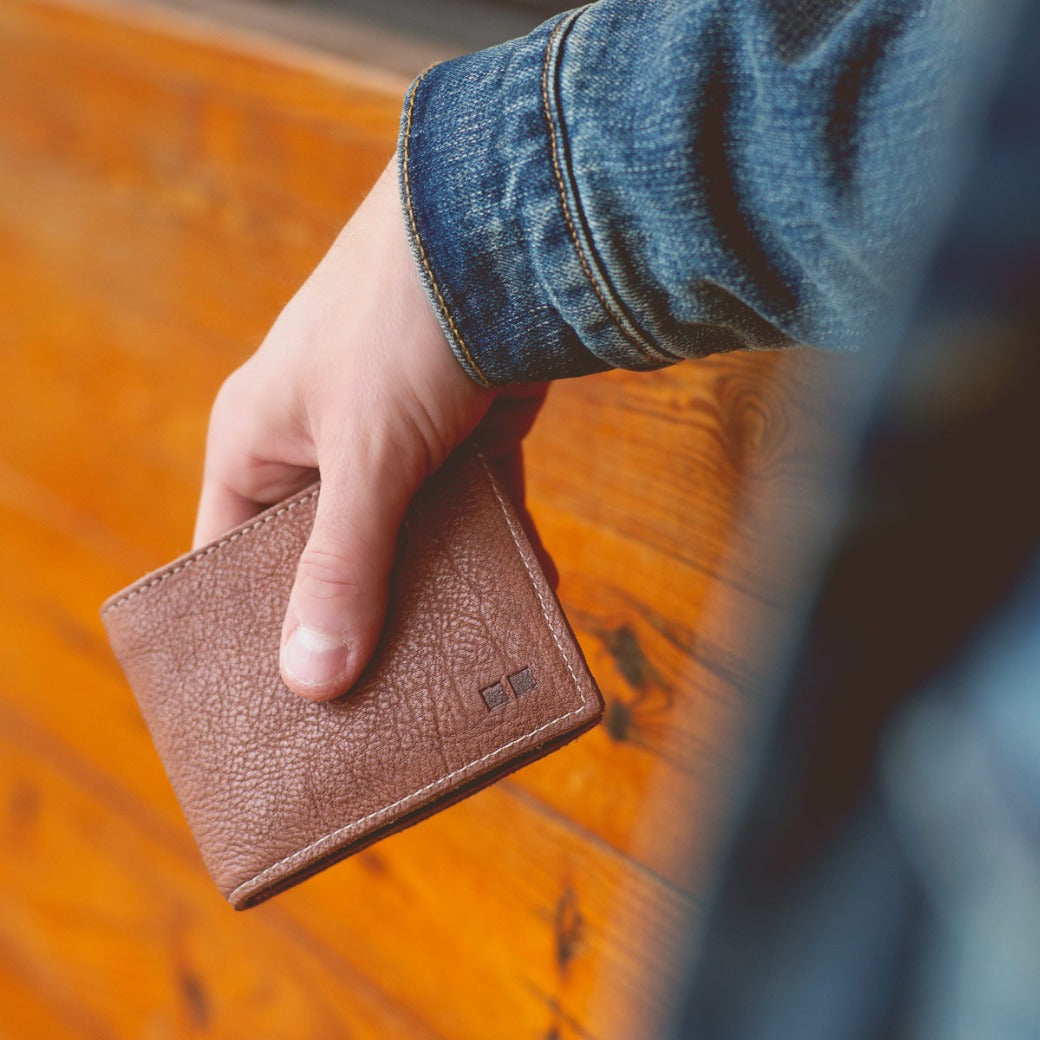 A person holding a Bed Stu Amidala wallet against a wooden wall.