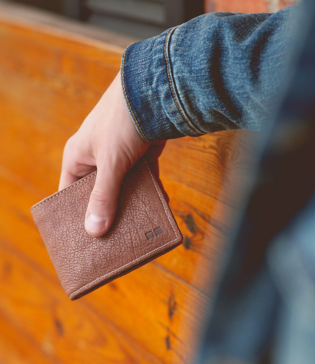A person holding a Bed Stu Amidala wallet against a wooden wall.