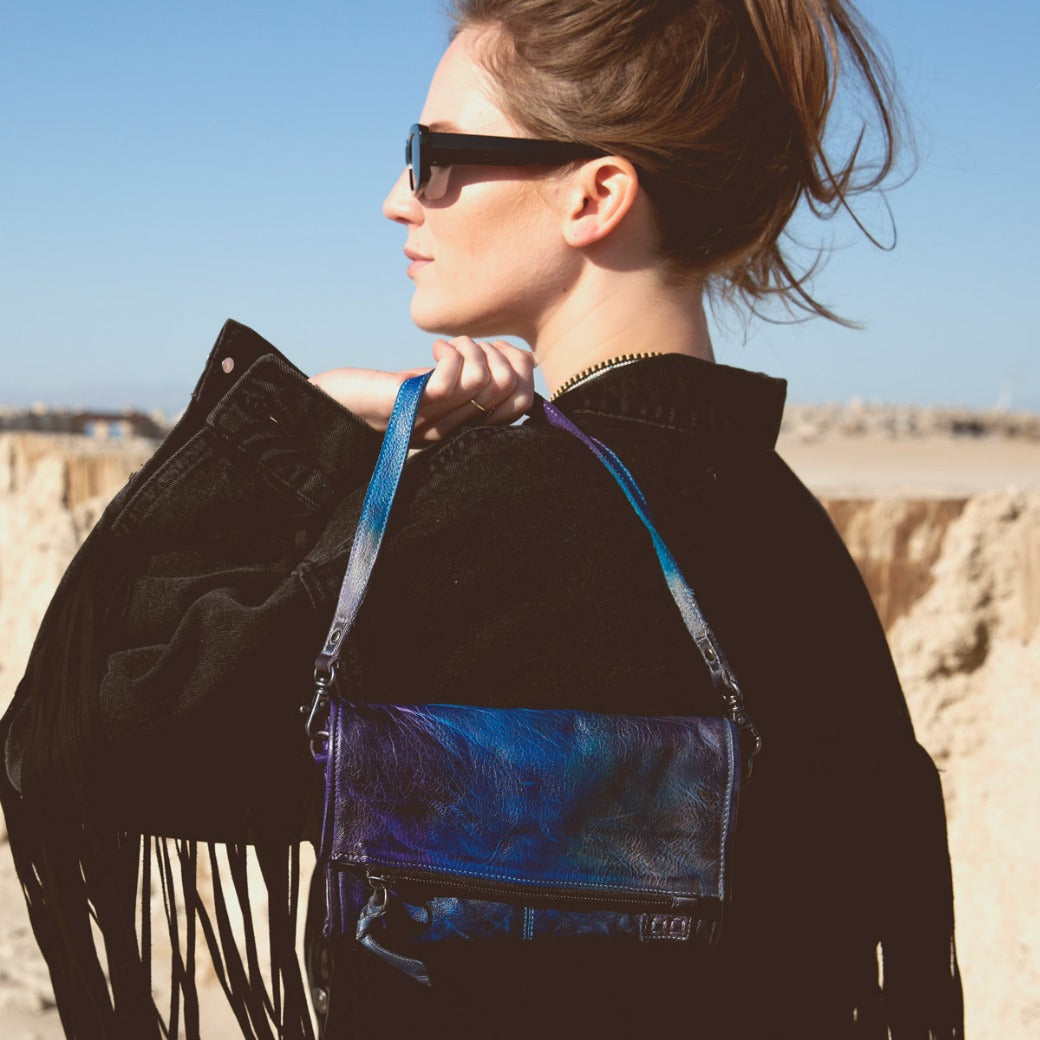 A woman is holding a blue and purple Bed Stu Amina handbag.