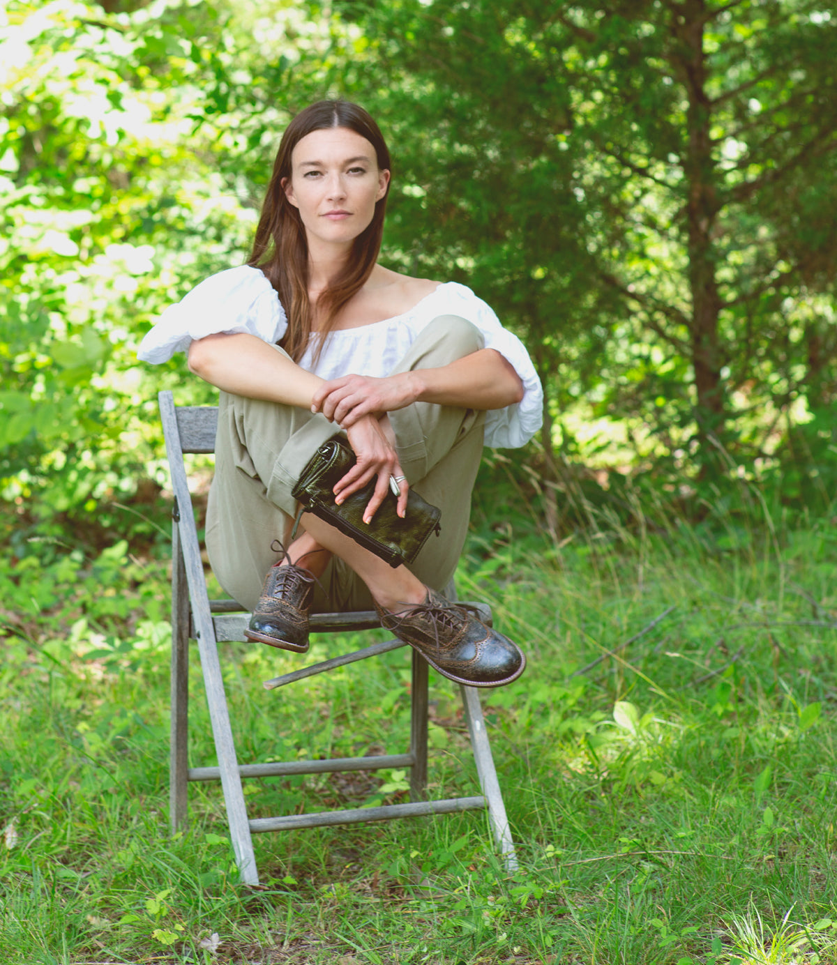 A woman sitting on a Bed Stu chair in the woods.