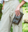 A woman wearing tan pants holding a Bed Stu leather wallet named Amina.
